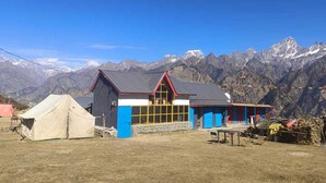 A mountain lodge with a large windowed room, a red roof, and a view of snow-capped mountains. - Grand Auli Camp (Joshimath)