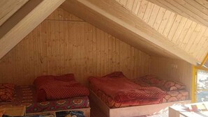 A cozy attic bedroom with wooden walls and sloped ceilings, featuring two beds with patterned bedding and a small table. - Grand Auli Camp (Joshimath)