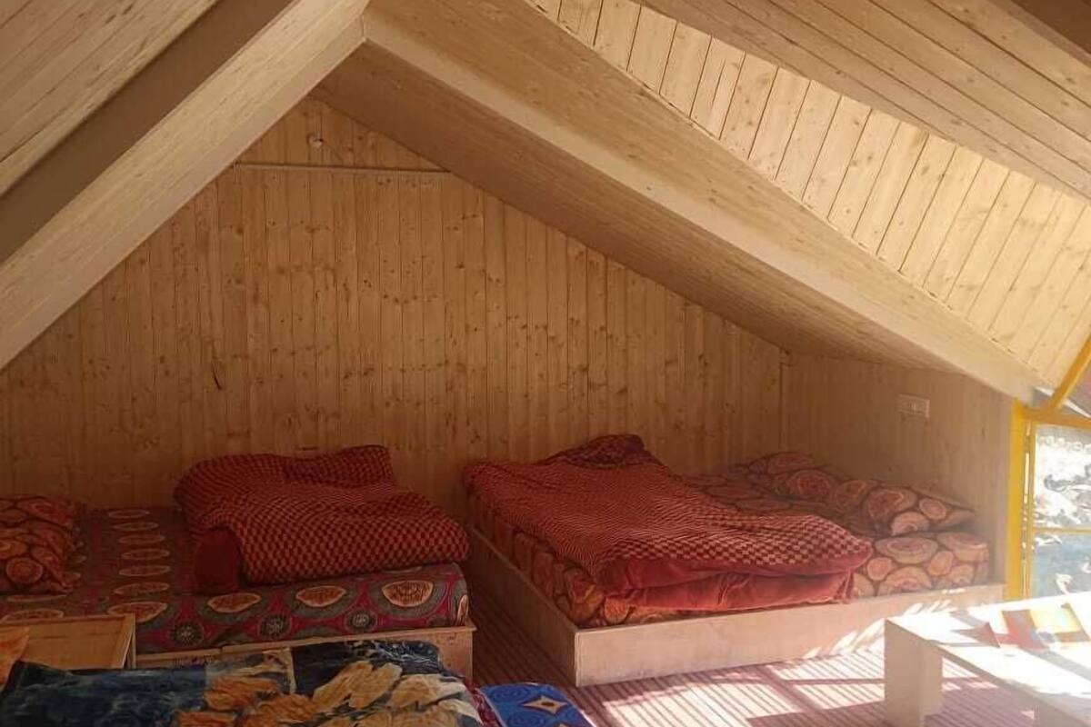 A cozy attic bedroom with wooden walls and sloped ceilings, featuring two beds with patterned bedding and a small table.