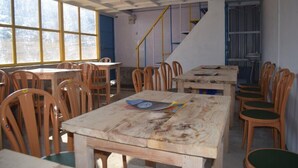 A classroom with wooden tables and chairs, large windows, and a staircase. - Grand Auli Camp (Joshimath)