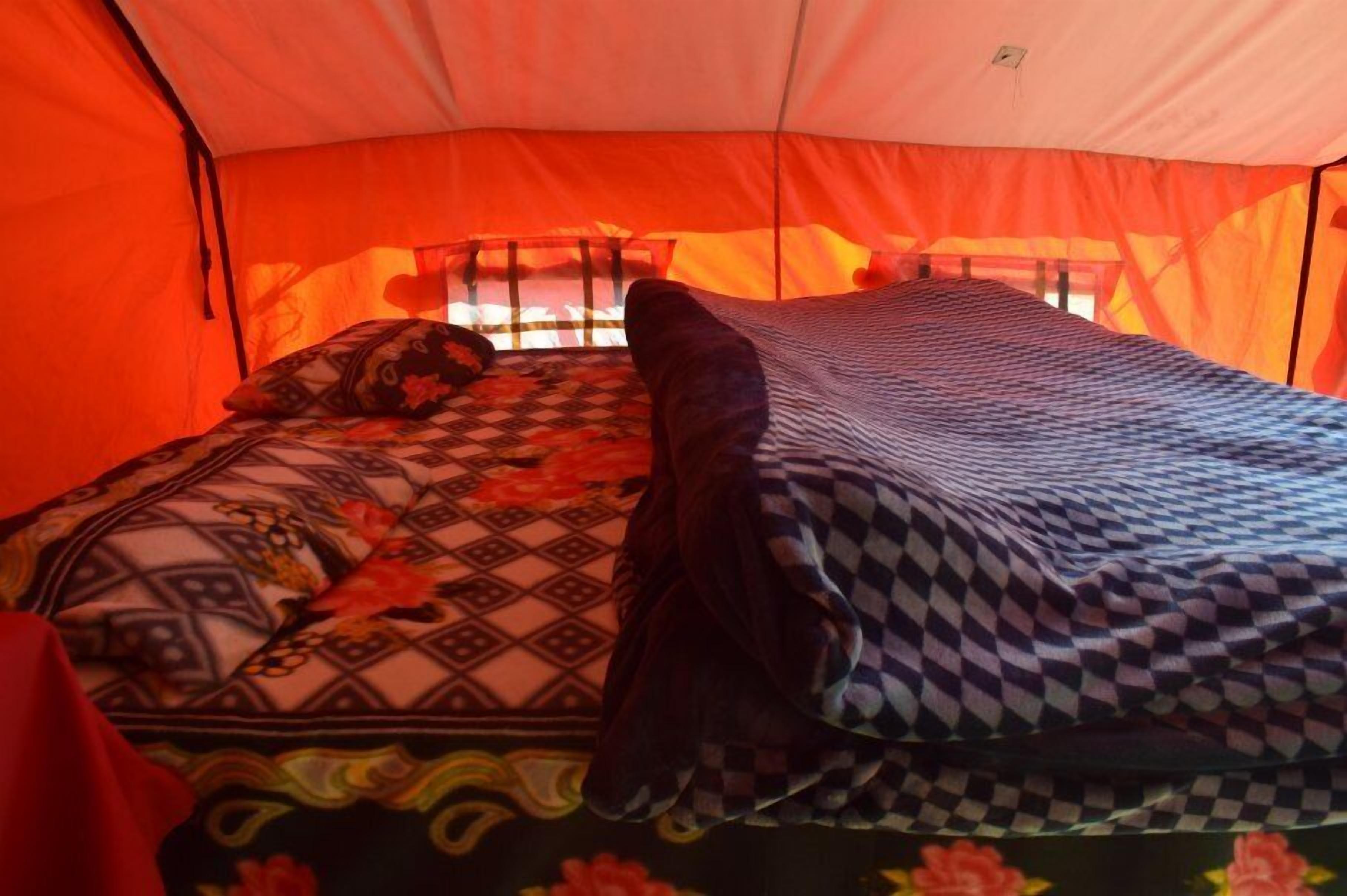 A tent with a bed inside, featuring patterned bedding and a window with a view.