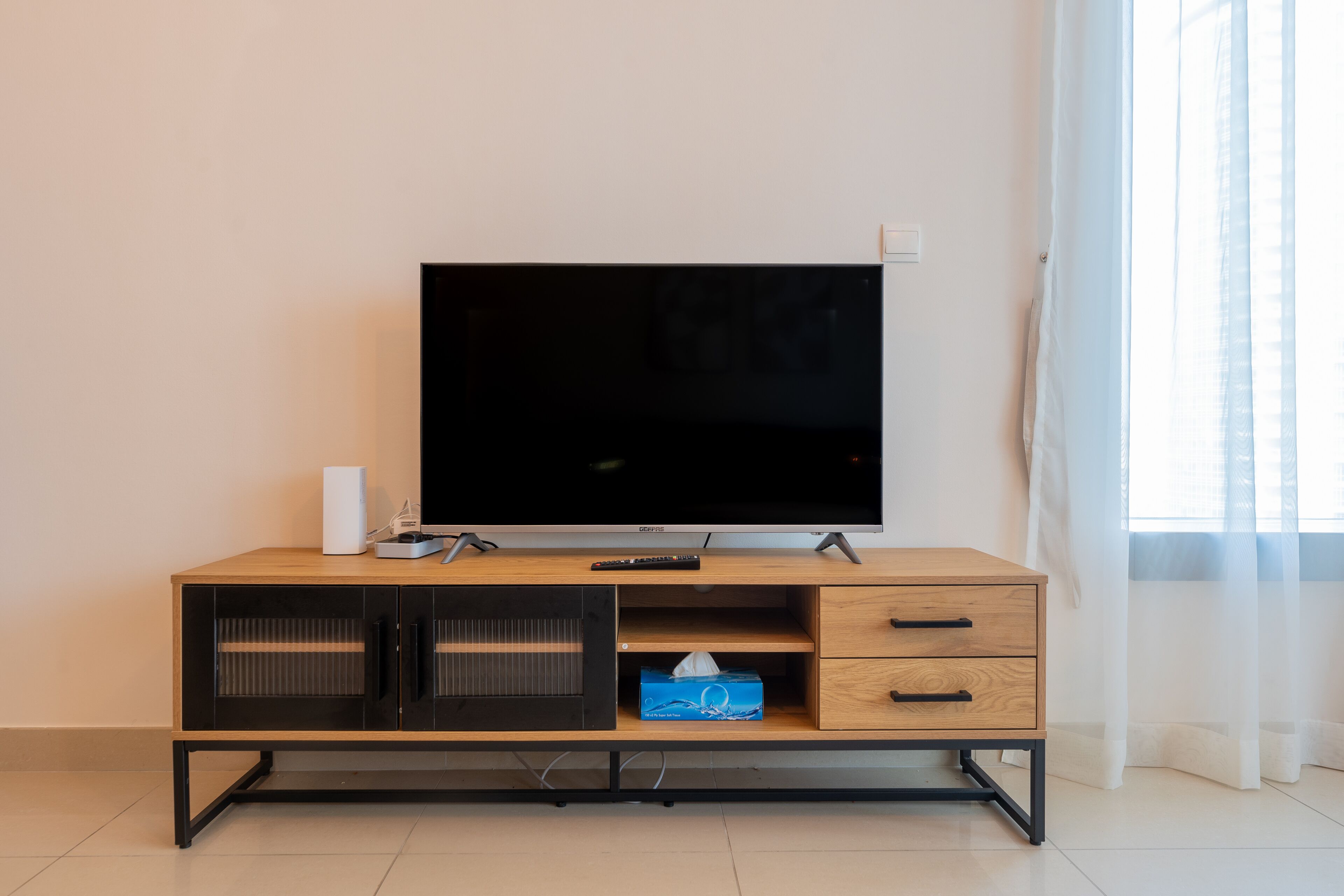 A modern living room with a flat-screen TV on a wooden TV stand, a remote control, and a tissue box.