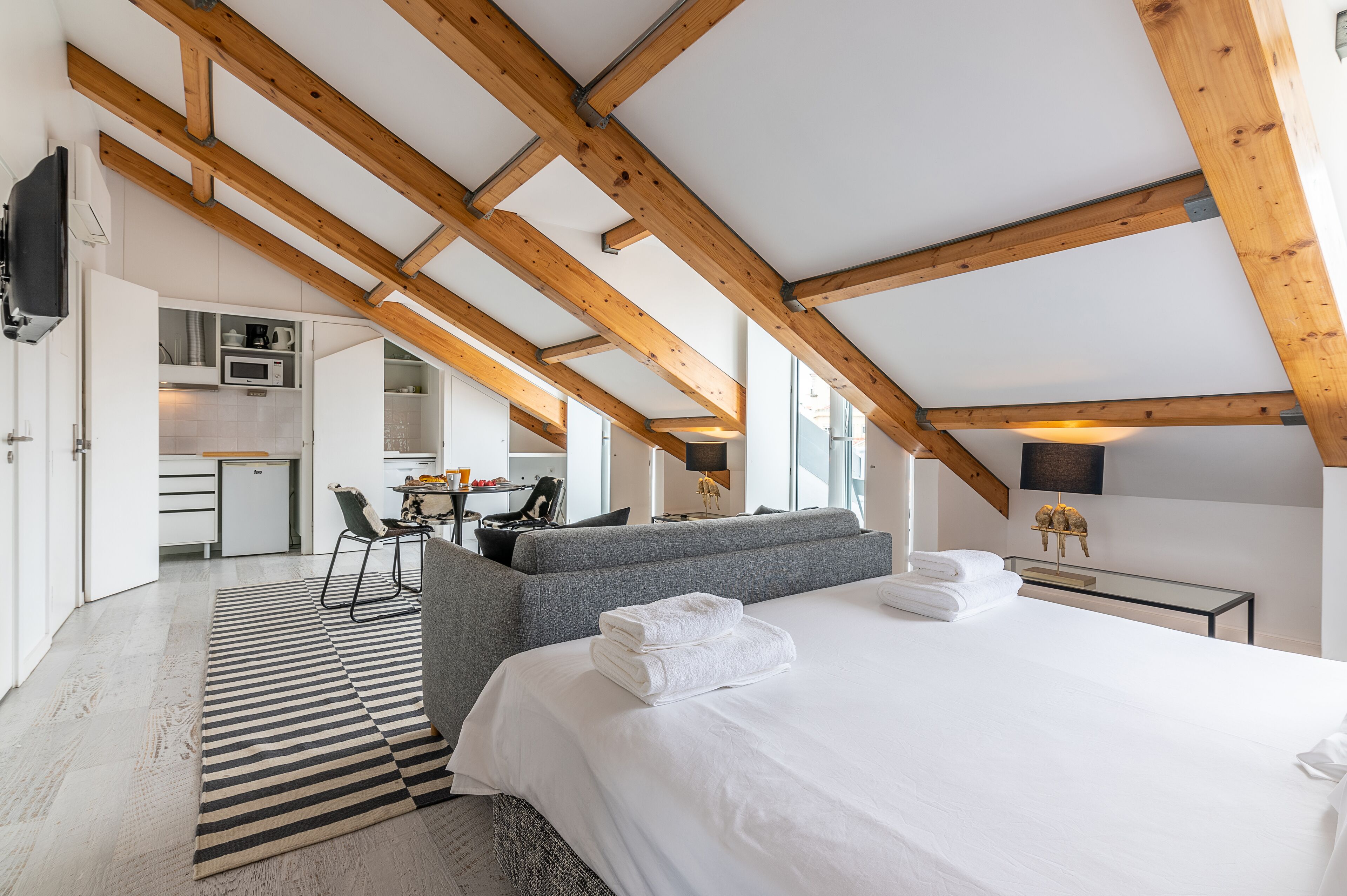 Ein modernes Hotelzimmer mit einer Schlafgalerie, einem großen Bett, einem grauen Sofa, einem Essbereich und einer Küchenzeile.