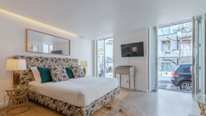 A bedroom with a bed, a TV, a window, and a view of the street. - Portas do Céu Apartments (Lisbon)
