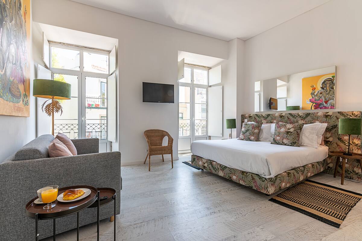 A modern hotel room with a bed, sofa, and a dining area with breakfast.