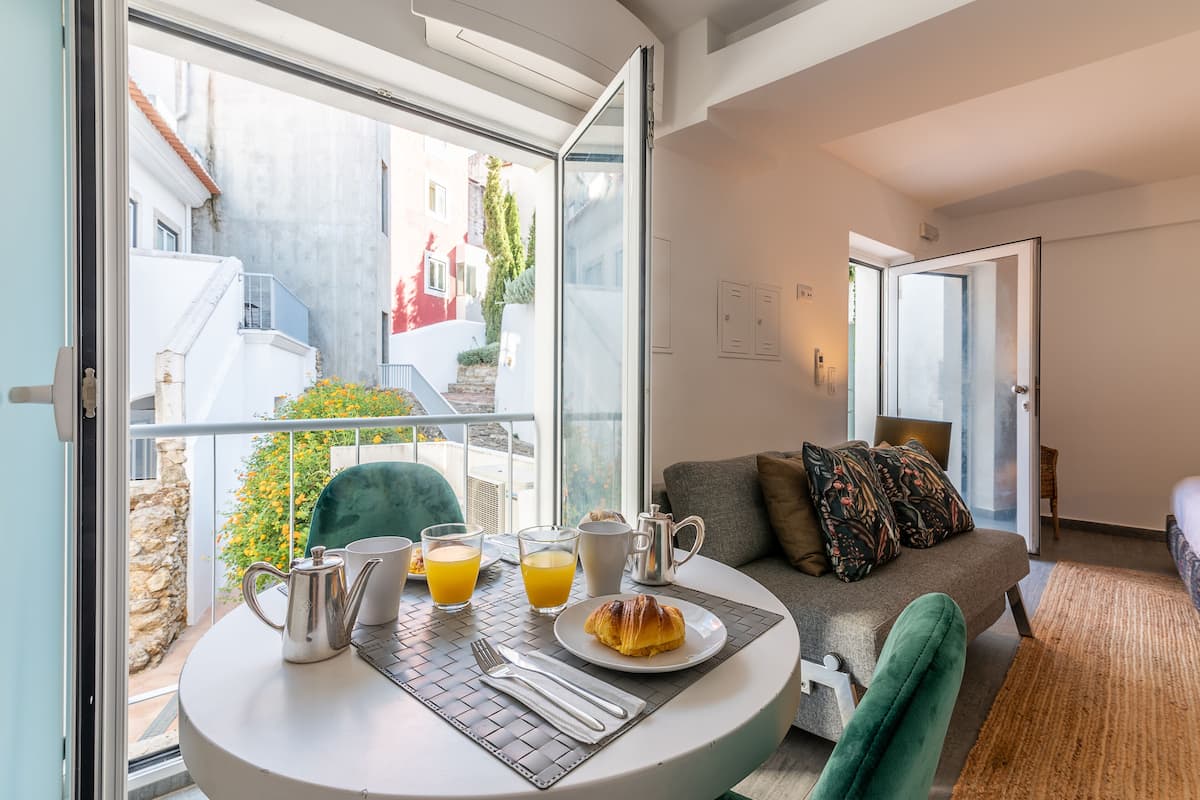 A balcony with a table set for breakfast, including a croissant, orange juice, and a coffee pot.