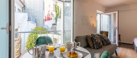 A balcony with a table set for breakfast, including a croissant, orange juice, and a coffee pot.
