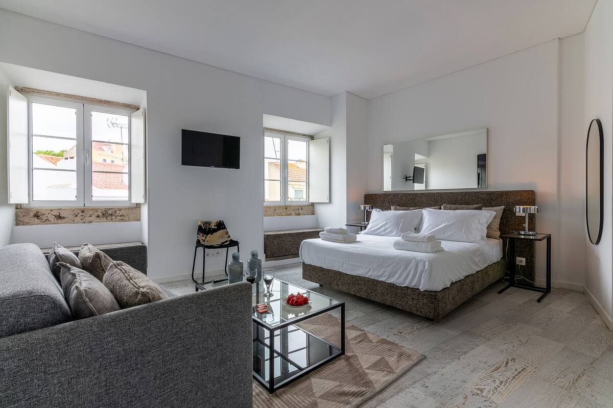 A modern bedroom with a large bed, a sofa, a coffee table, and a TV mounted on the wall.