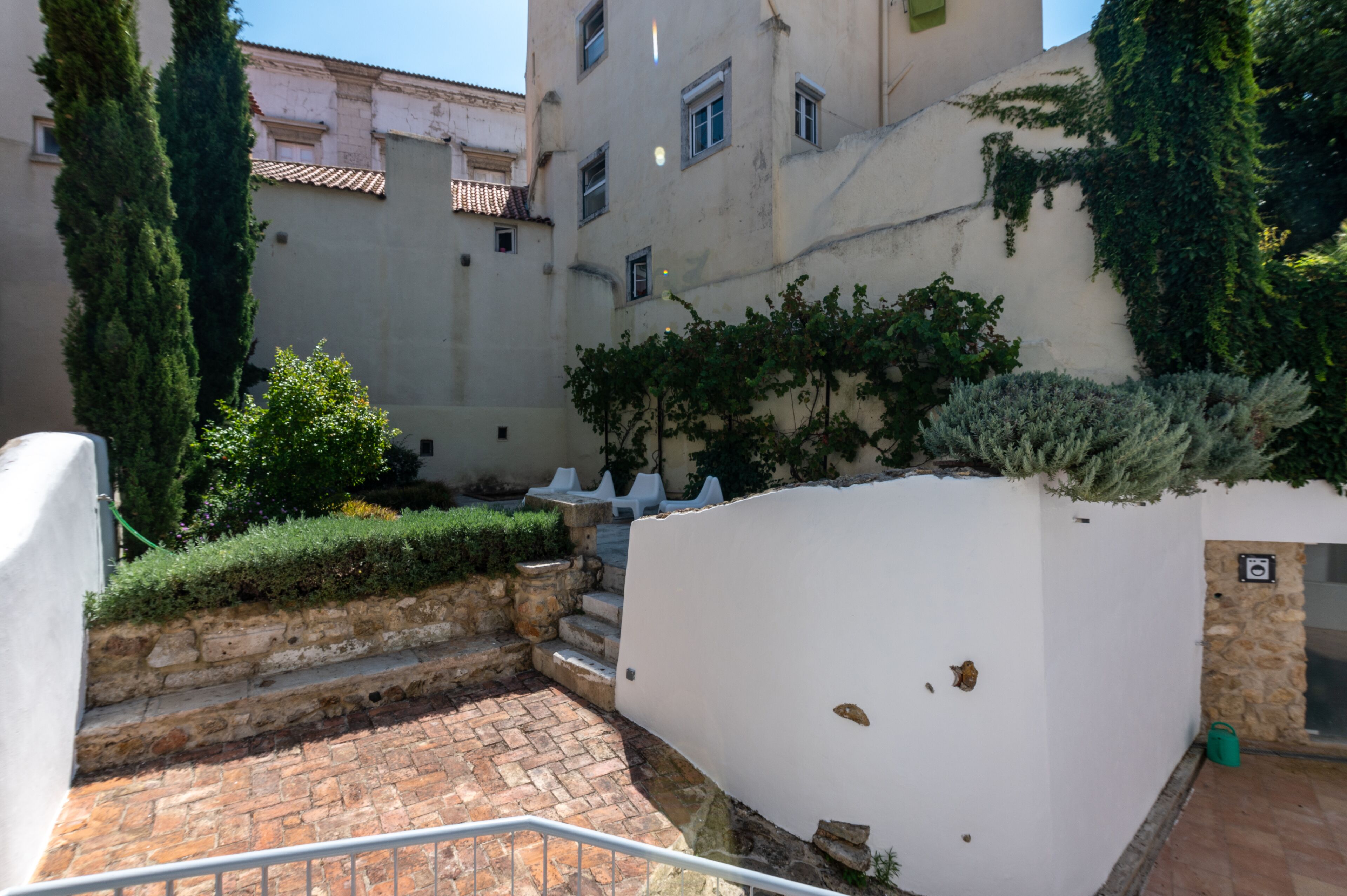 A courtyard with stone steps, white walls, and greenery.