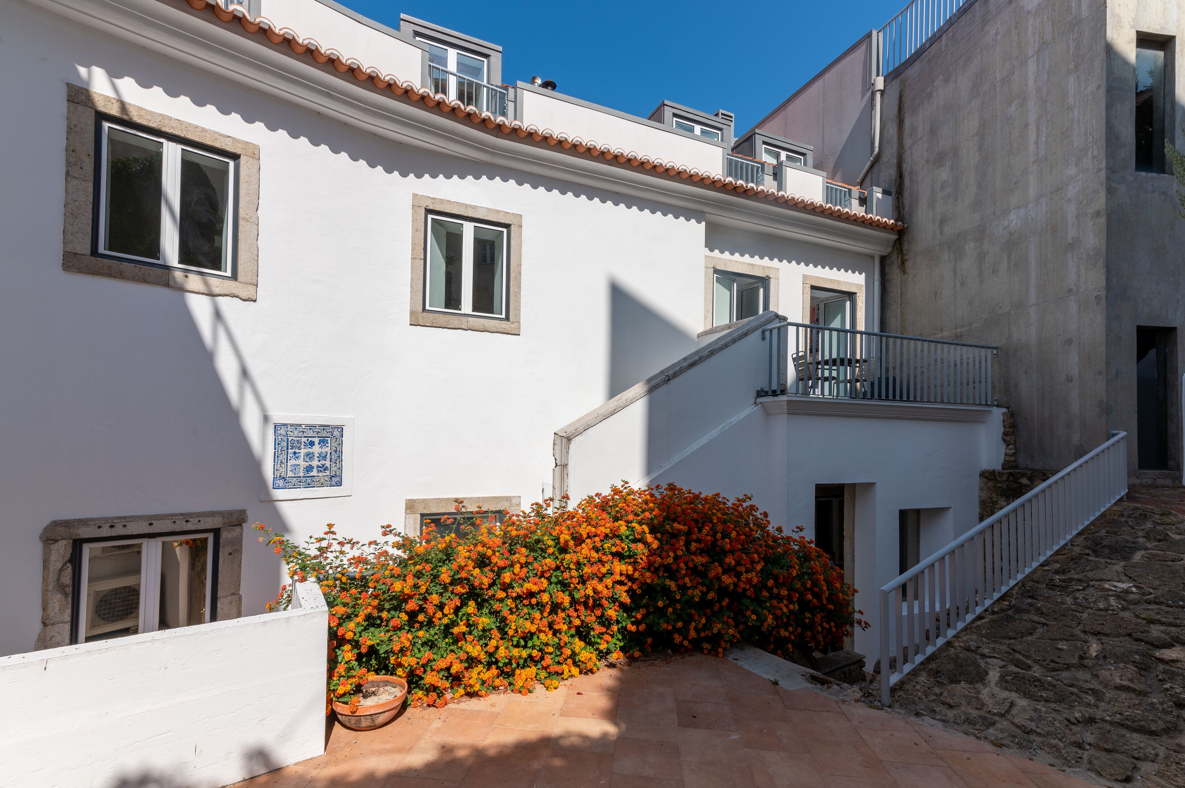 A white building with a tiled roof, a small balcony, and a stone staircase leading to the entrance.