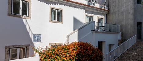 A white building with a tiled roof, a small balcony, and a stone staircase leading to the entrance.