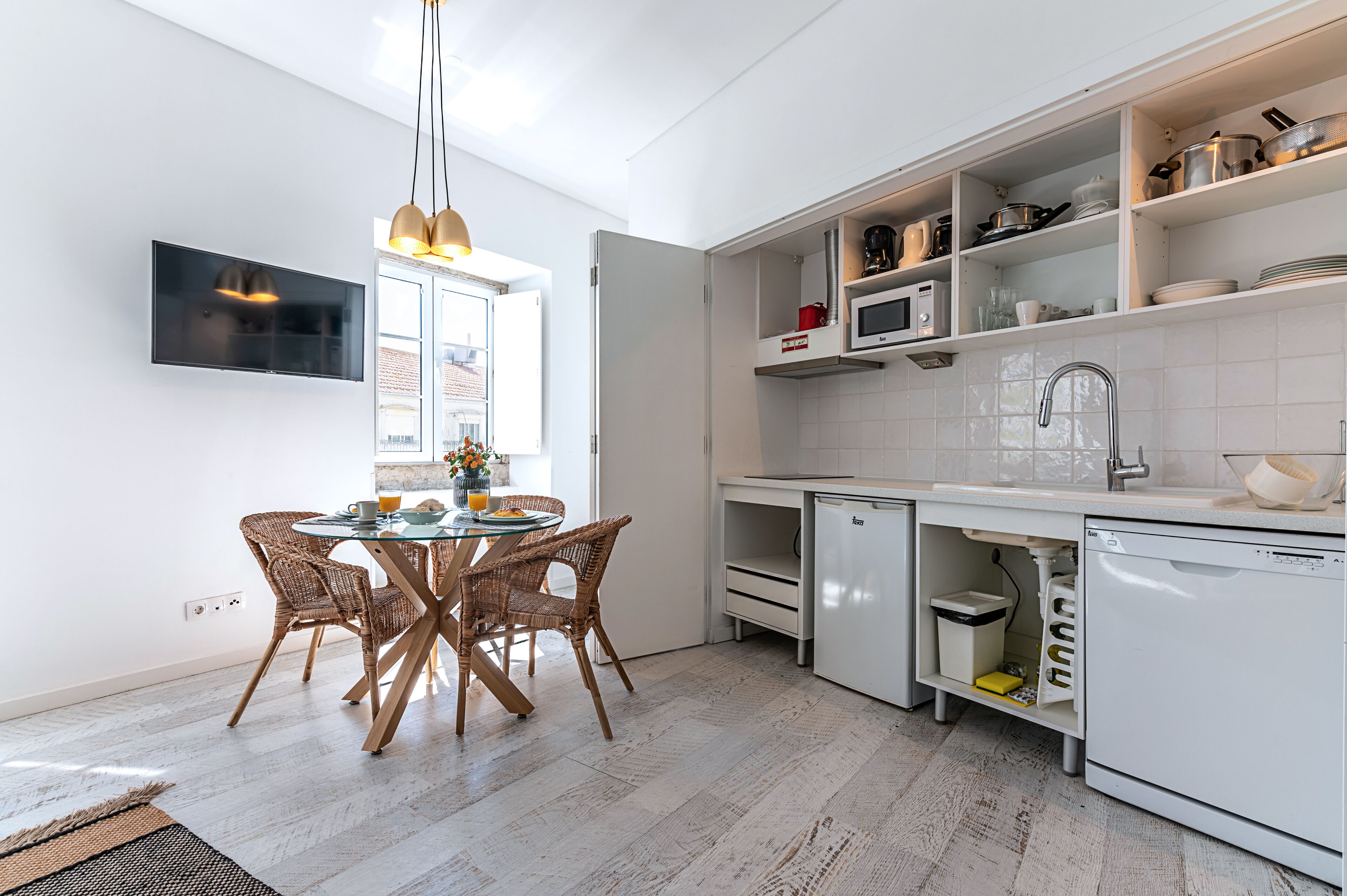 A modern kitchen with white cabinetry, a dining table with wicker chairs, a built-in microwave, and a large window.