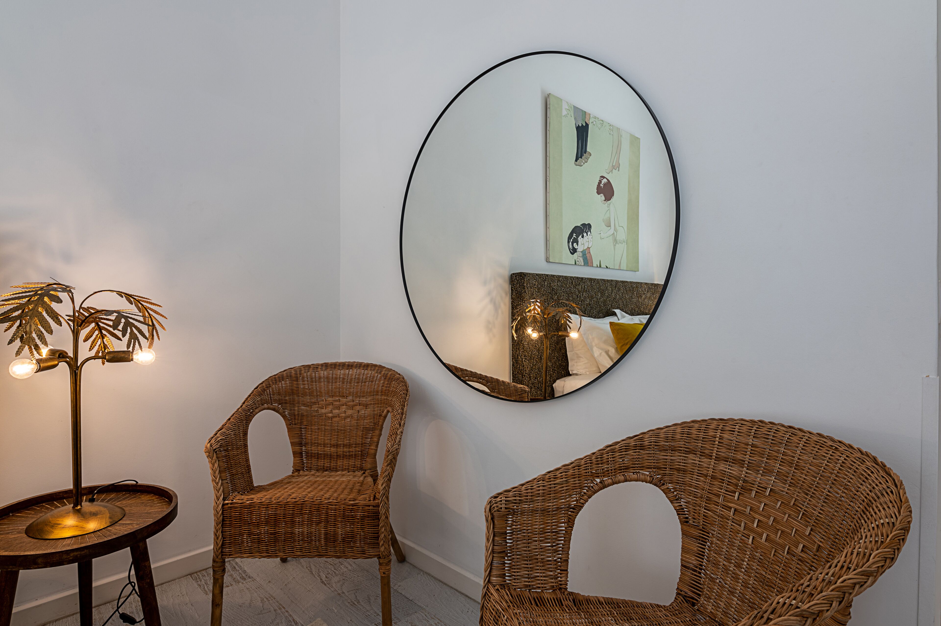 A room with two wicker chairs, a round mirror, and a floor lamp.