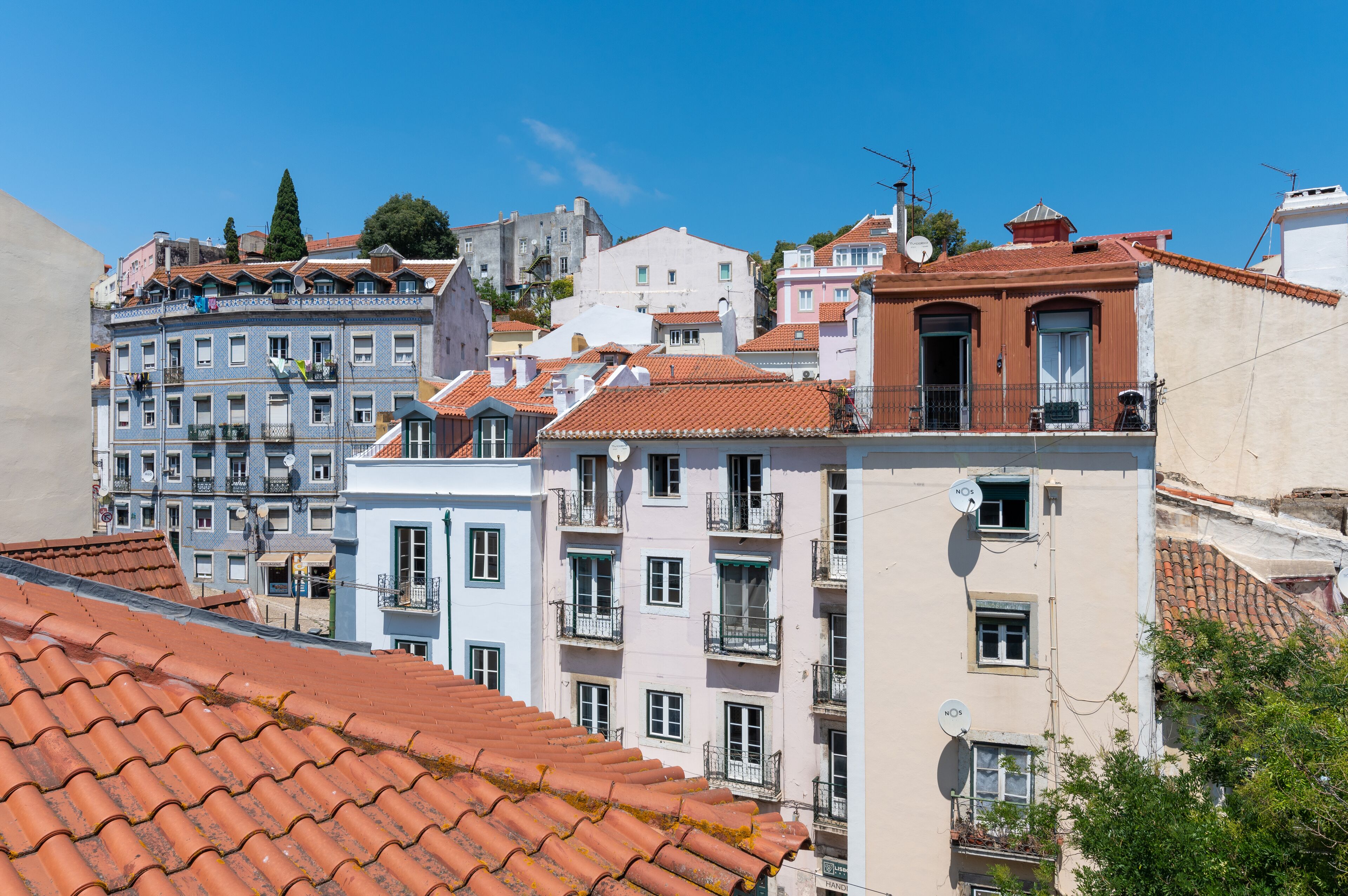 A row of multi-story buildings with red-tiled roofs, balconies, and satellite dishes.