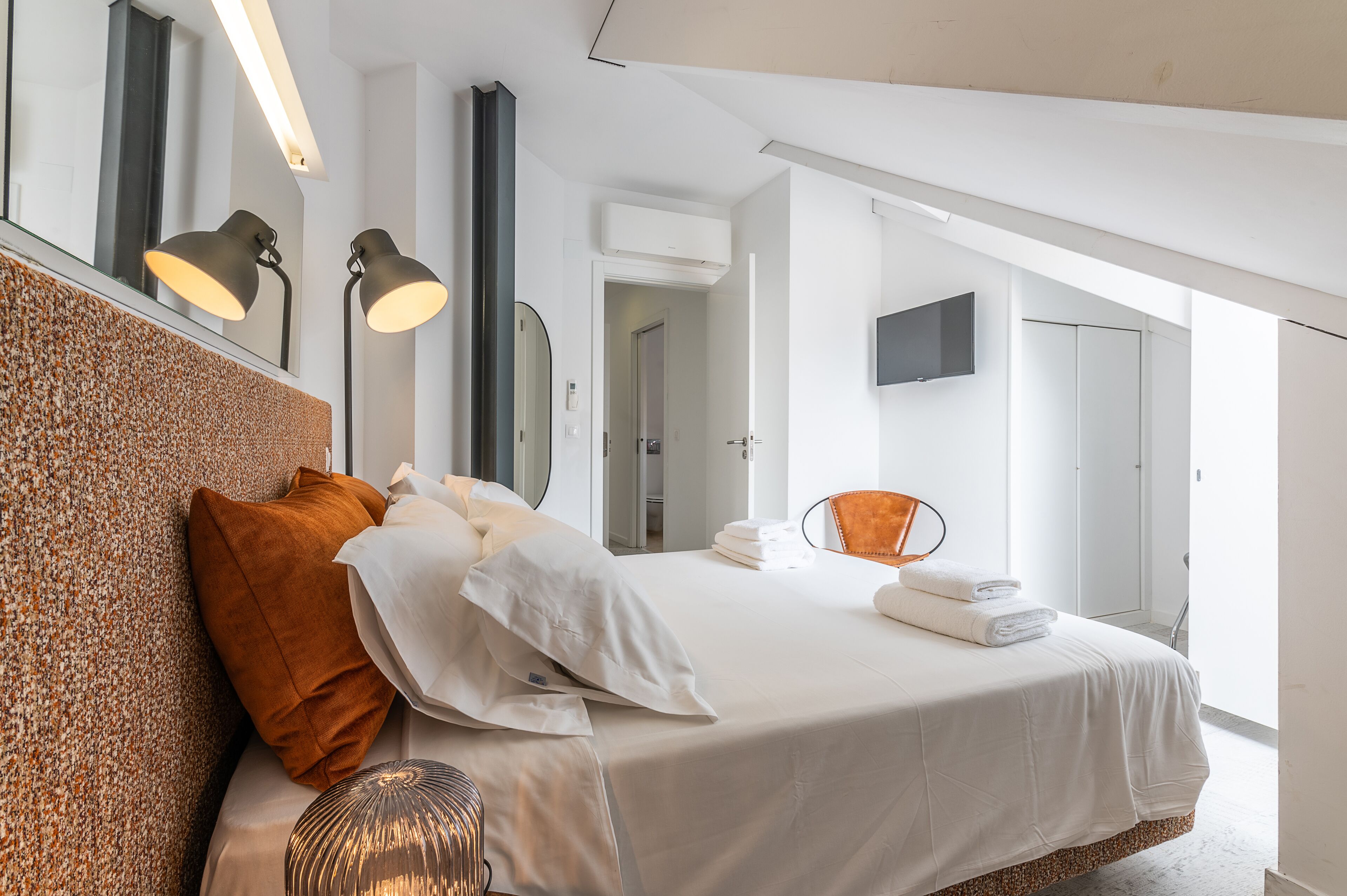 Una habitación de hotel moderna con una cama grande, una zona de estar con una silla, un televisor de pantalla plana y un ventanal que ofrece vistas al exterior.