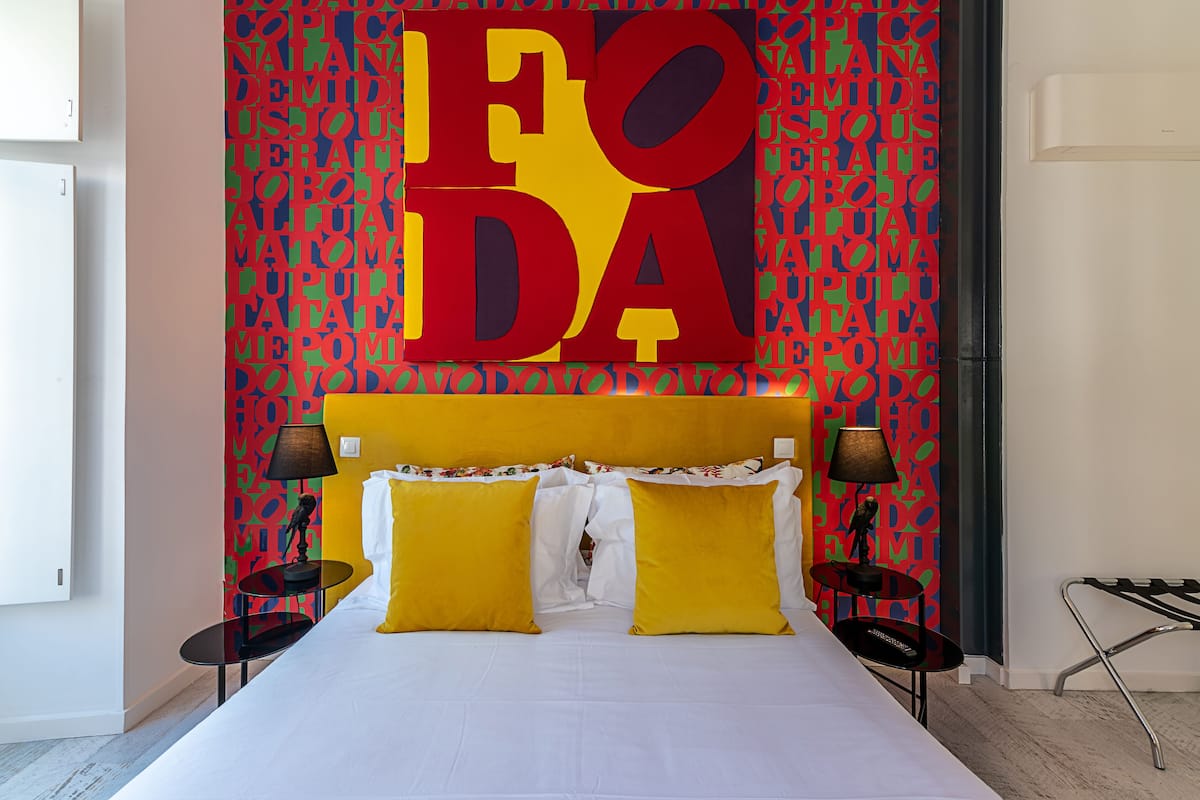 A hotel room with a large bed, two bedside tables, and a colorful wall with the word "FODA" prominently displayed.