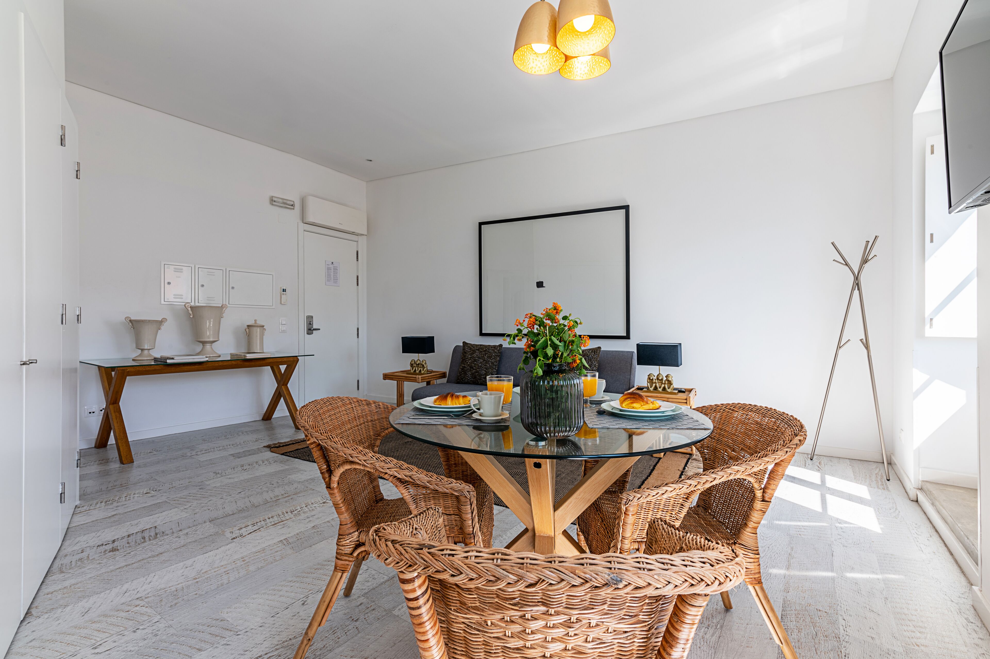 A modern dining area with wicker chairs, a glass table, and a vase of flowers.