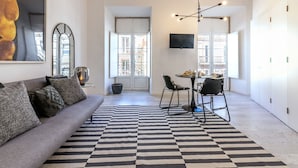 A modern living room with a sofa, a dining table with chairs, a black and white striped rug, and a TV mounted on the wall. - Portas do Céu Apartments (Lisbon)
