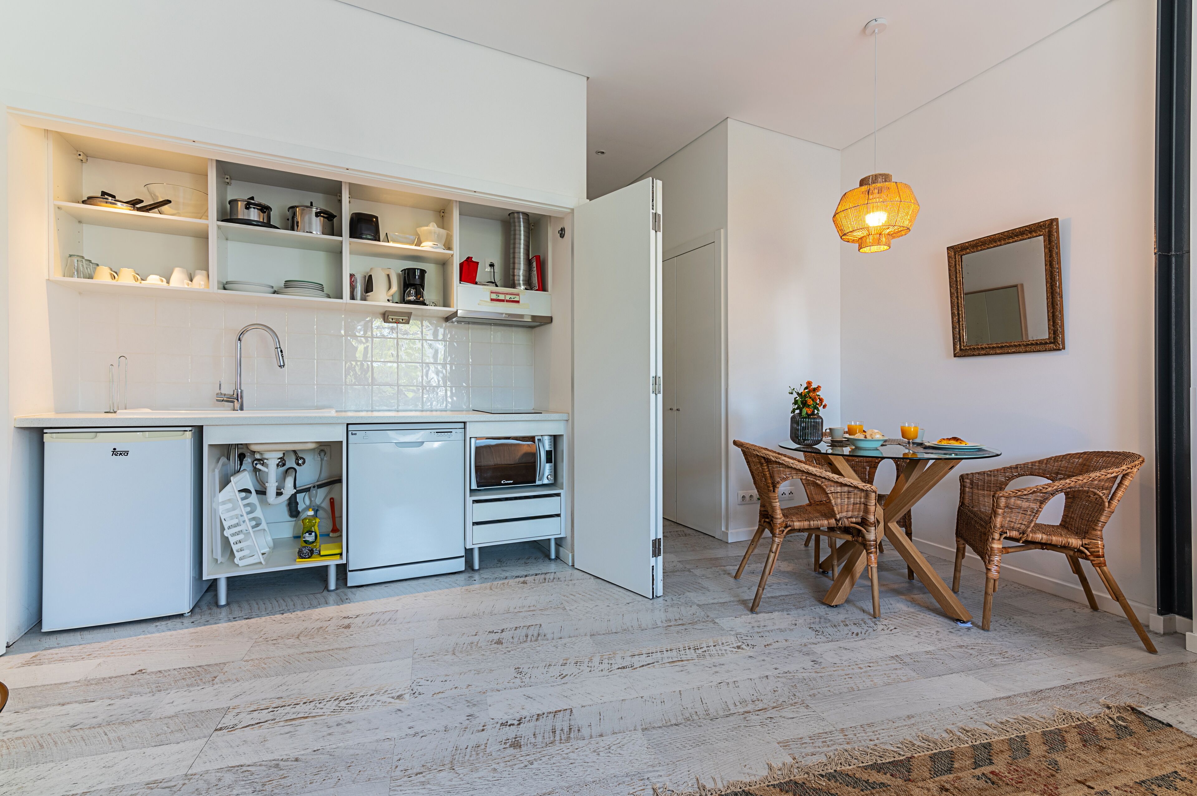 Een moderne keuken met witte kasten, een geïntegreerde vaatwasser en een eethoek met rieten stoelen en een glazen tafel.