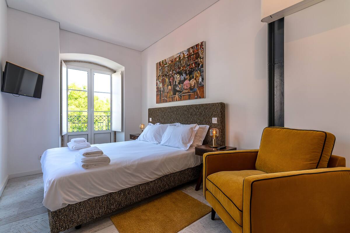 A bedroom with a bed, a television, a painting, and a window.