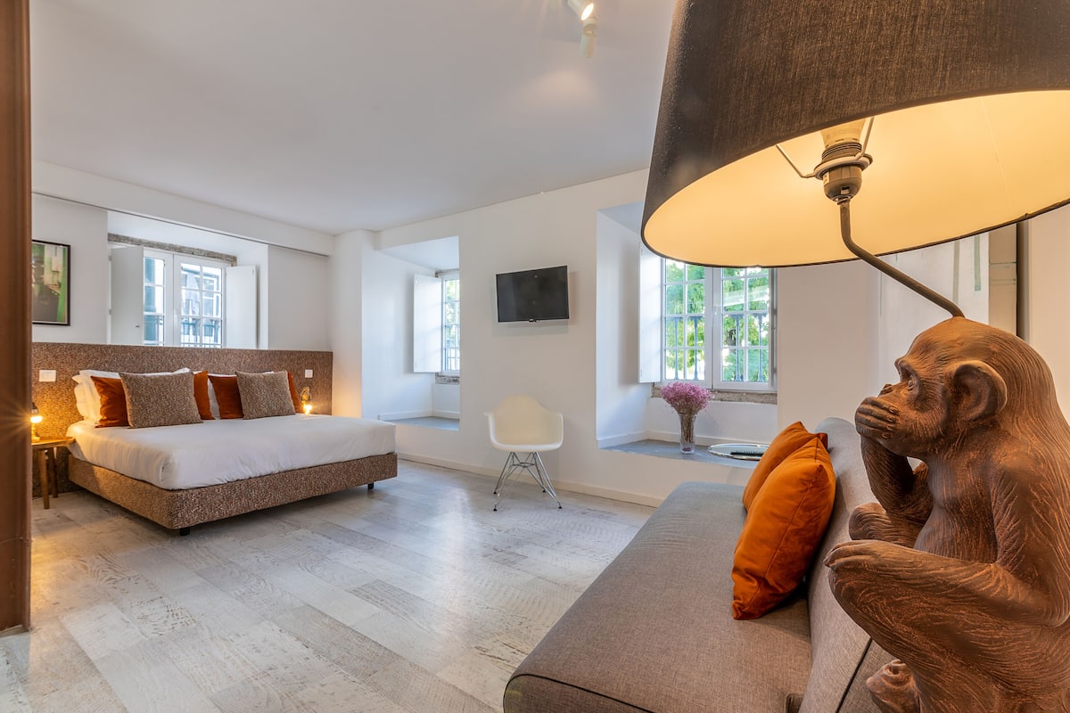 A modern bedroom with a bed, a sofa, a chair, a TV, and a large window.