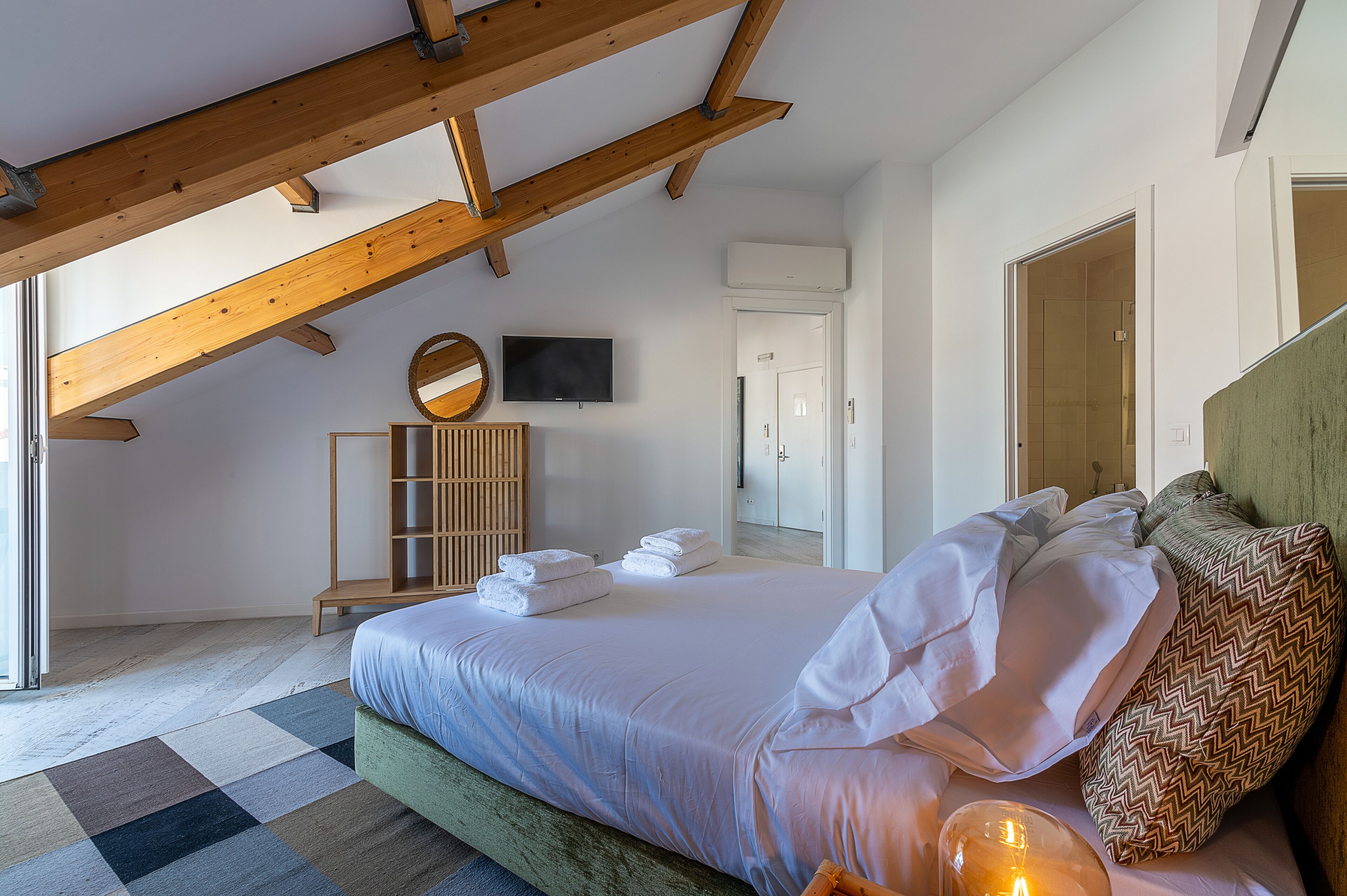 Camera da letto con un letto, soffitto in legno, televisione, armadio e porta del bagno.