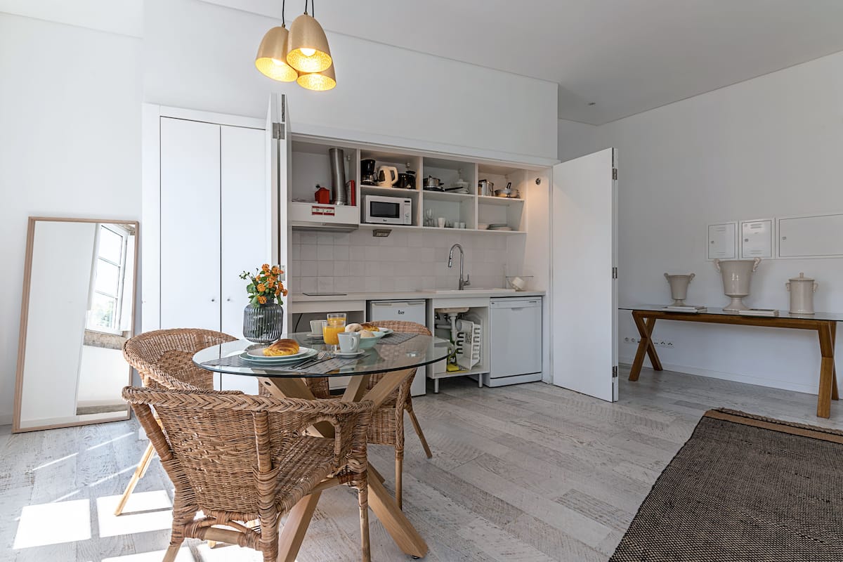 A modern kitchen with white cabinetry, a glass dining table, wicker chairs, and a hanging light fixture.