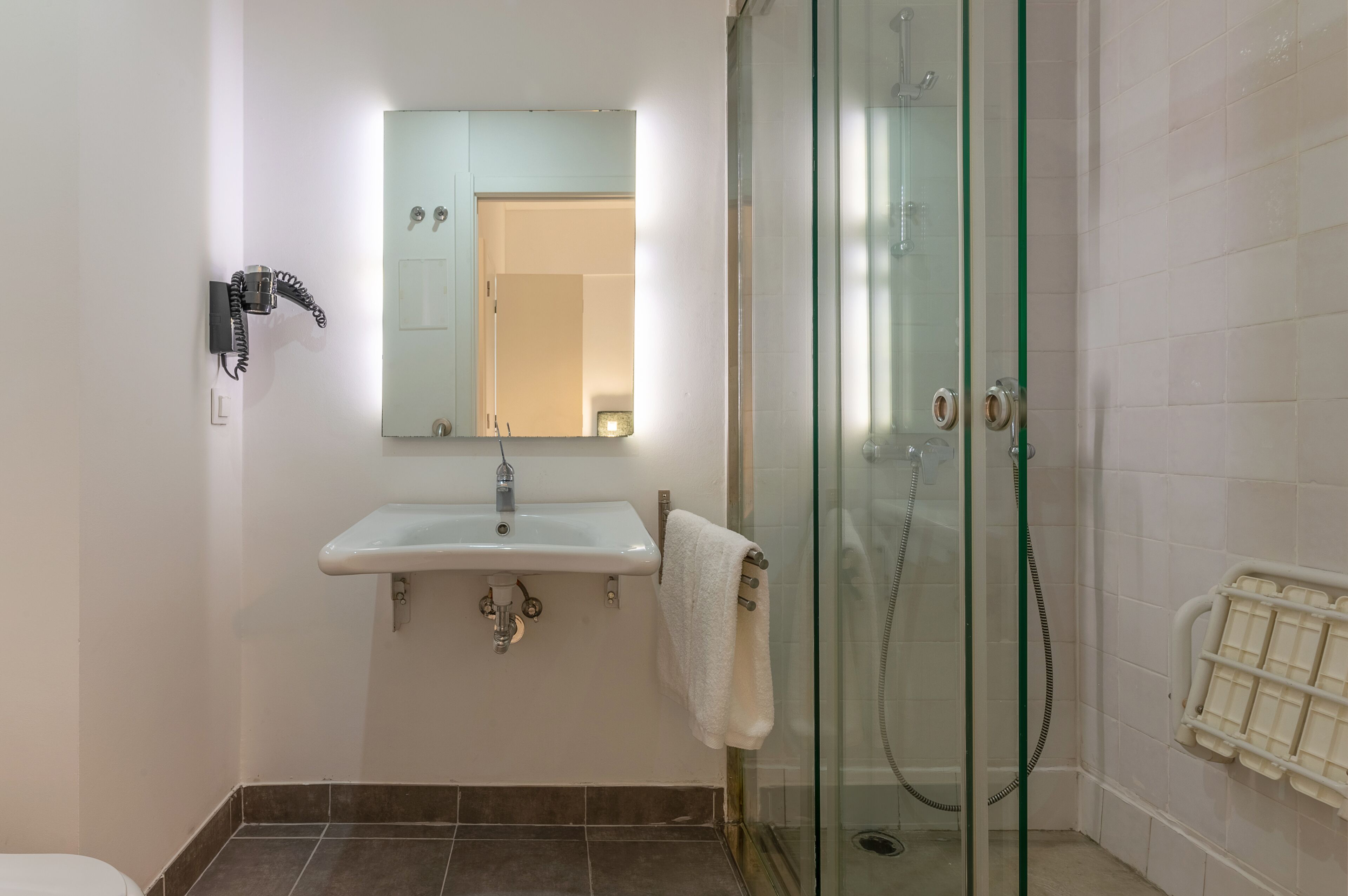A bathroom with a glass-enclosed shower, a white sink with a mirror above it, and a towel hanging on the wall.