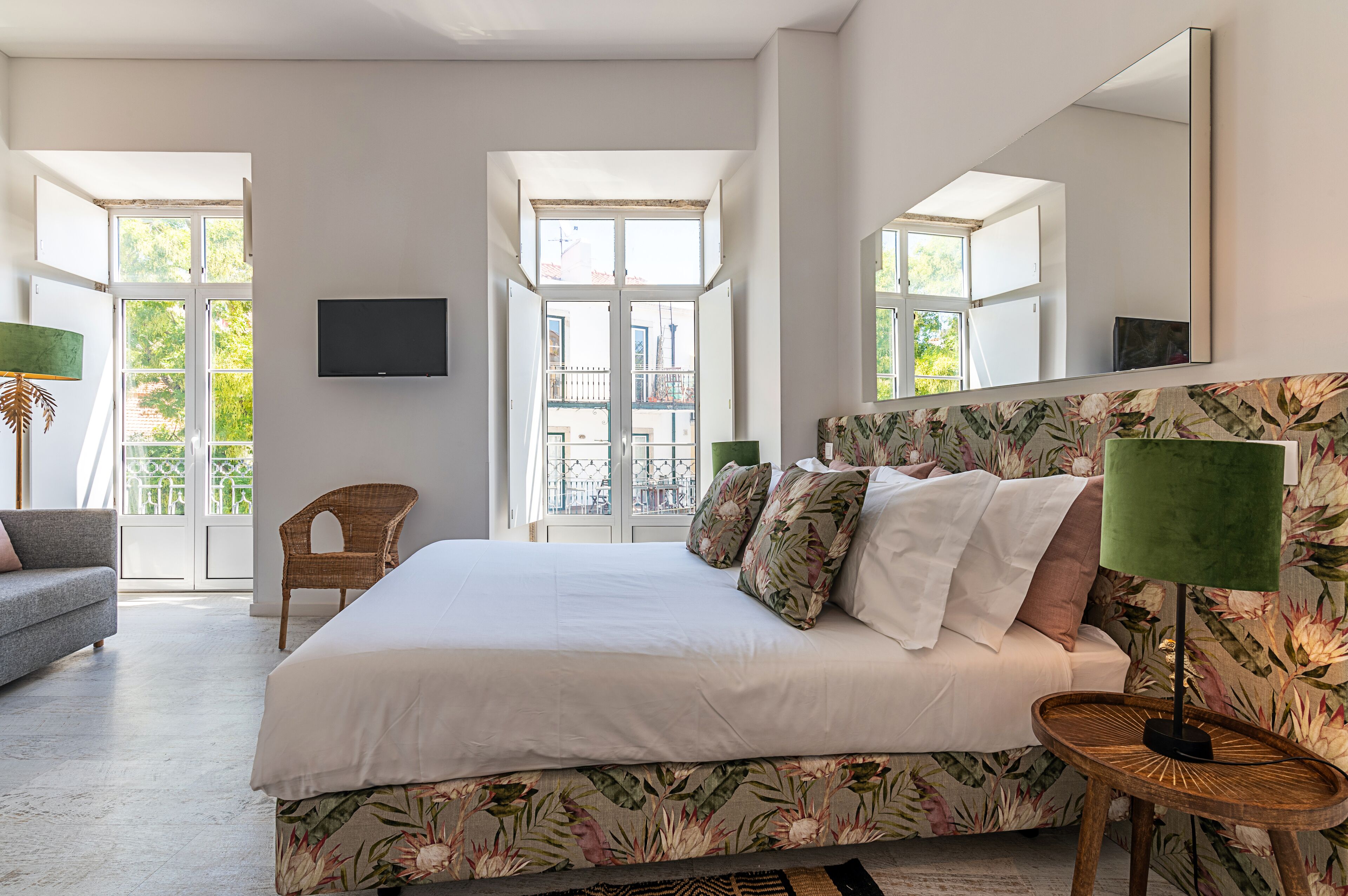 A spacious bedroom with a large bed, a flat-screen TV, and a balcony with a view of the city.