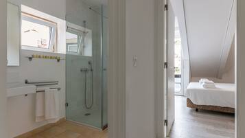 Un baño moderno con ducha de vidrio, lavamanos blanco y un perchero para toallas.