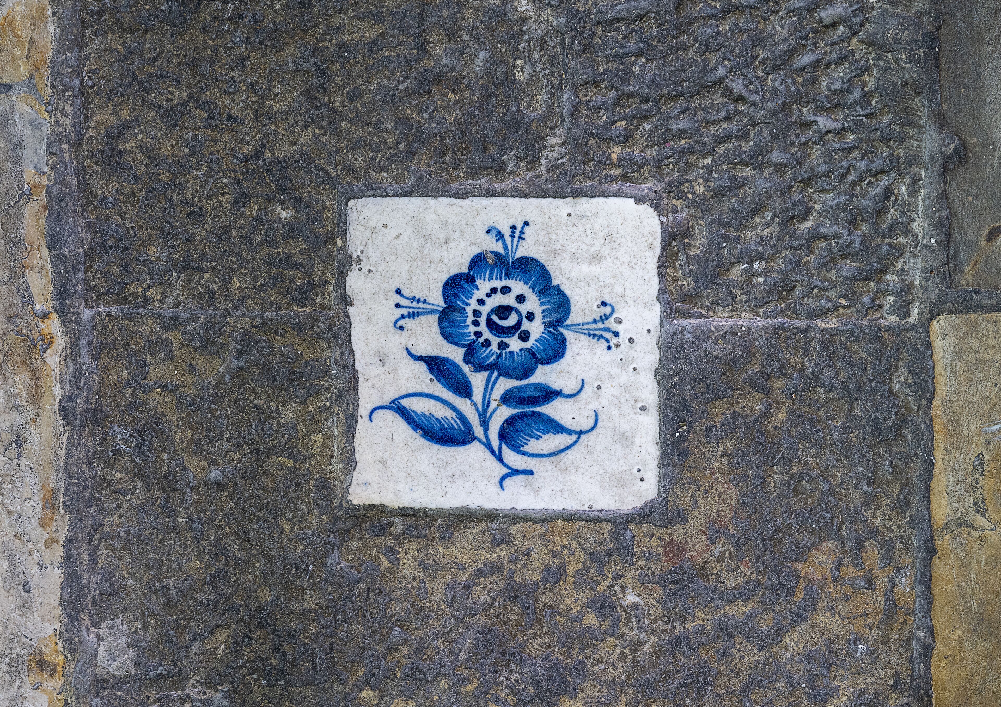 A tile with a blue floral design on a stone wall.