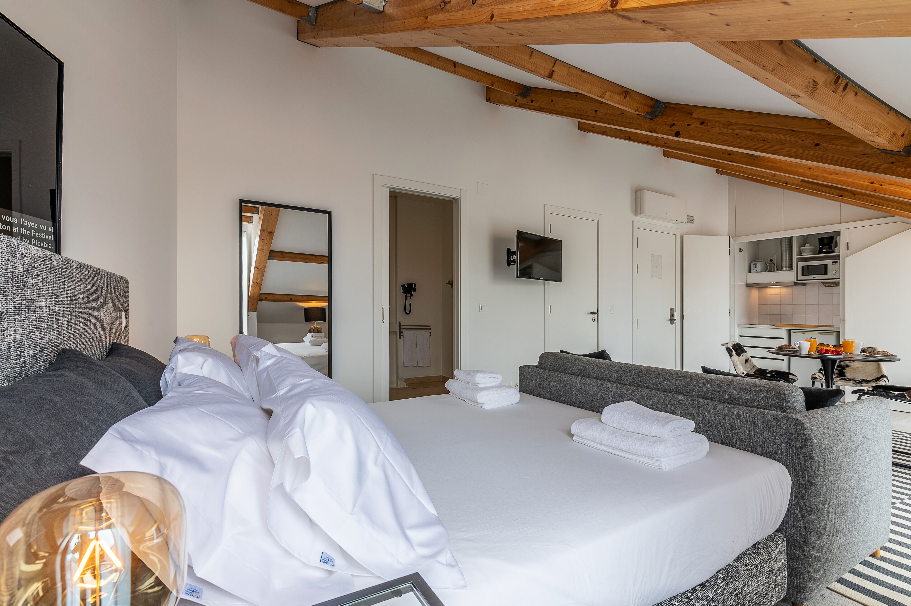 A hotel room with a large bed, a sofa, a television, and a kitchenette.