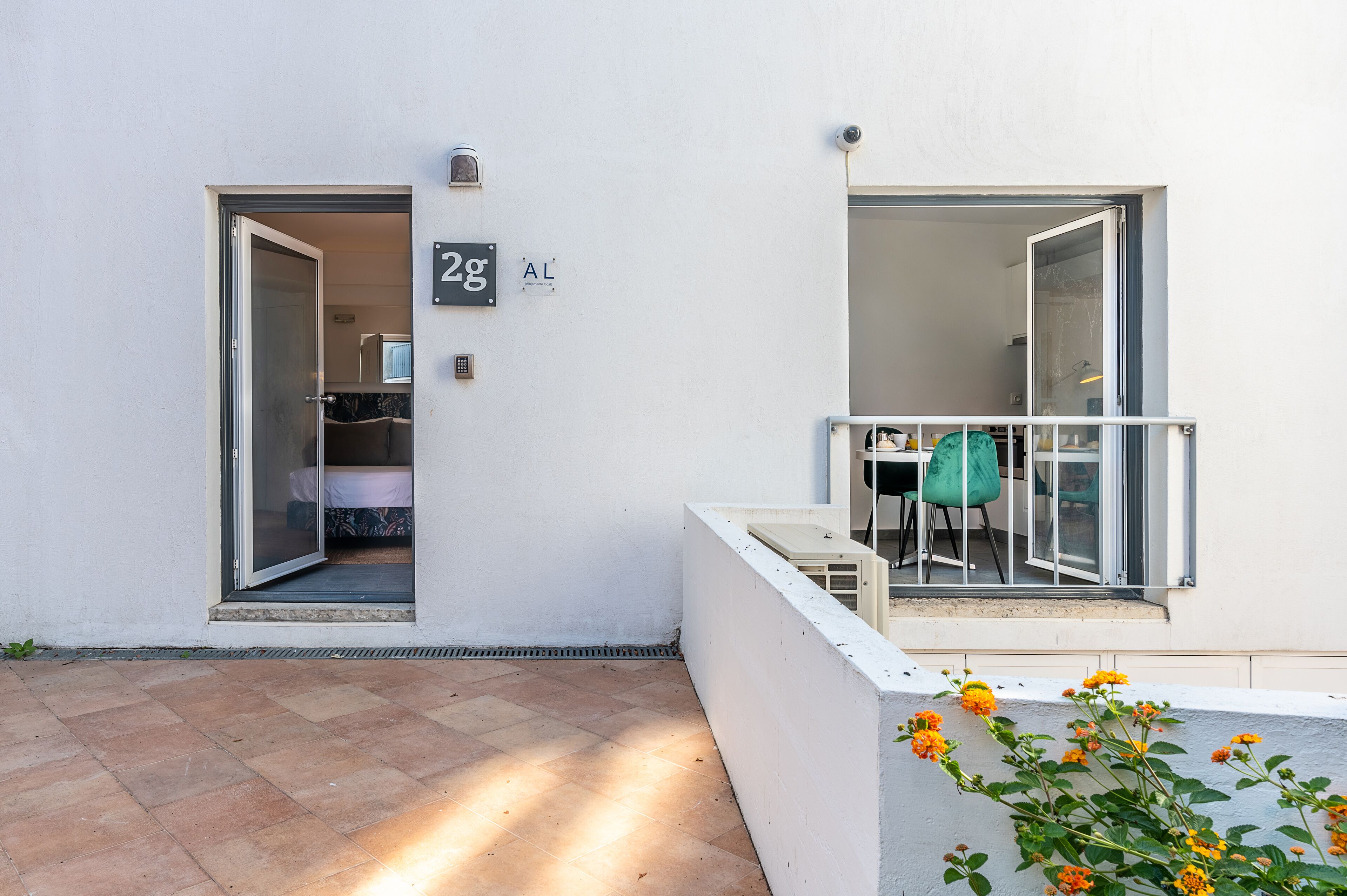 Eine moderne Wohnung mit Glastürschieberausgang, einem Balkon mit weißer Brüstung und einer kleinen Sitzgelegenheit im Freien.