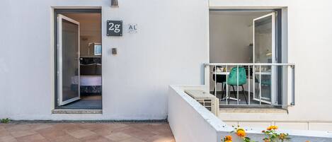 Eine moderne Wohnung mit Glastürschieberausgang, einem Balkon mit weißer Brüstung und einer kleinen Sitzgelegenheit im Freien.