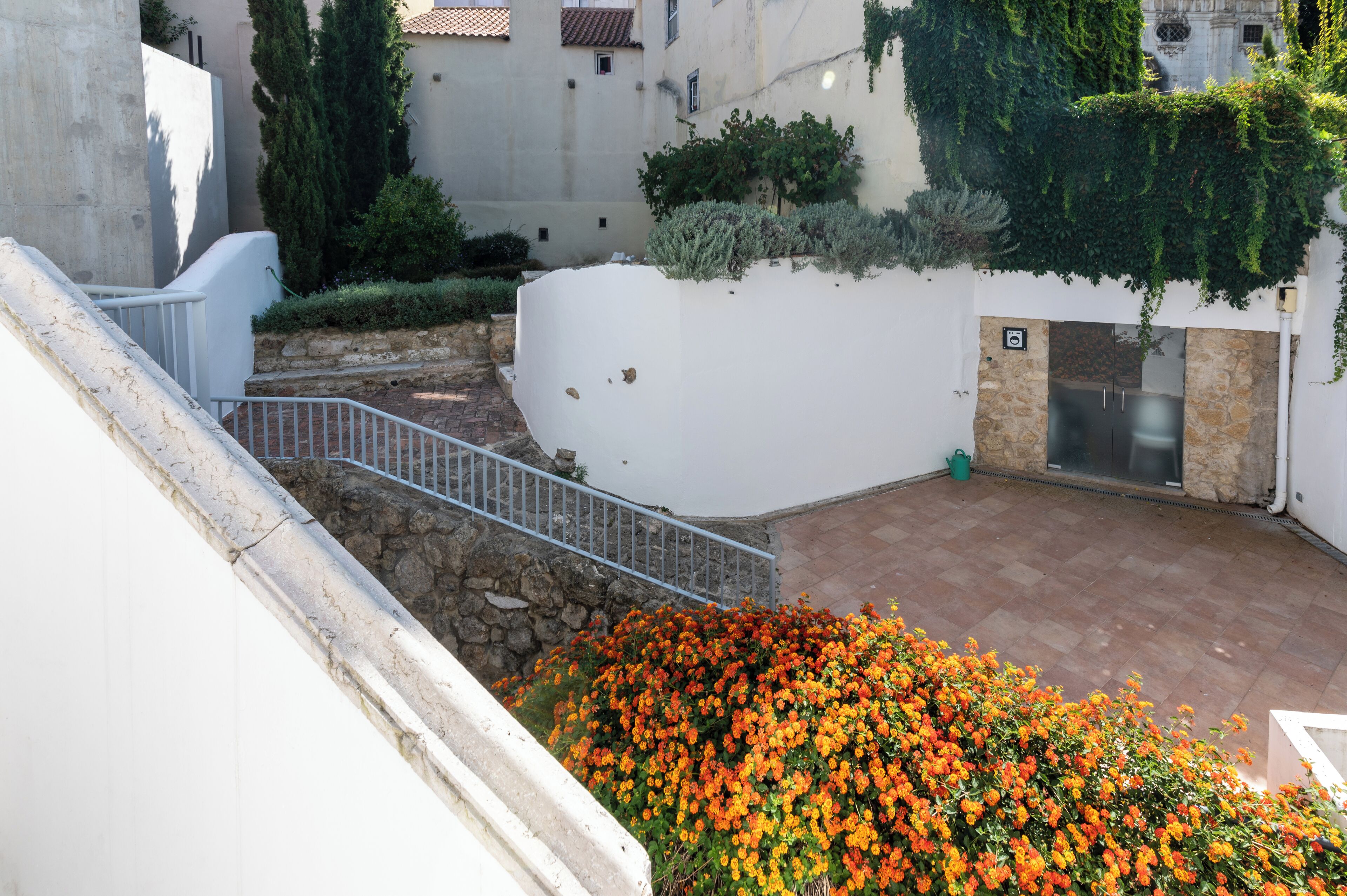 A courtyard with a stone wall, a metal railing, and a flower bed.