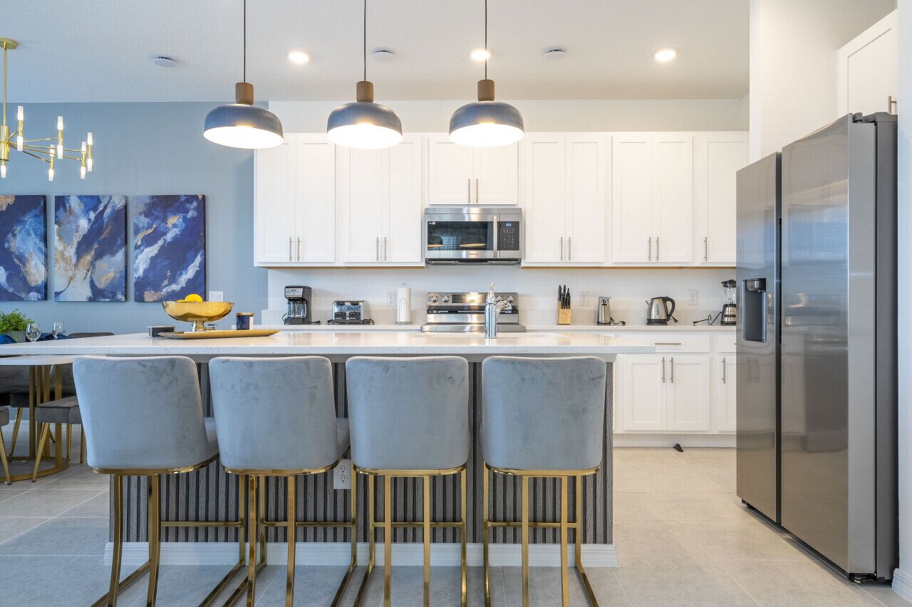 A modern kitchen with white cabinets, a stainless steel refrigerator, and a bar area with grey chairs.