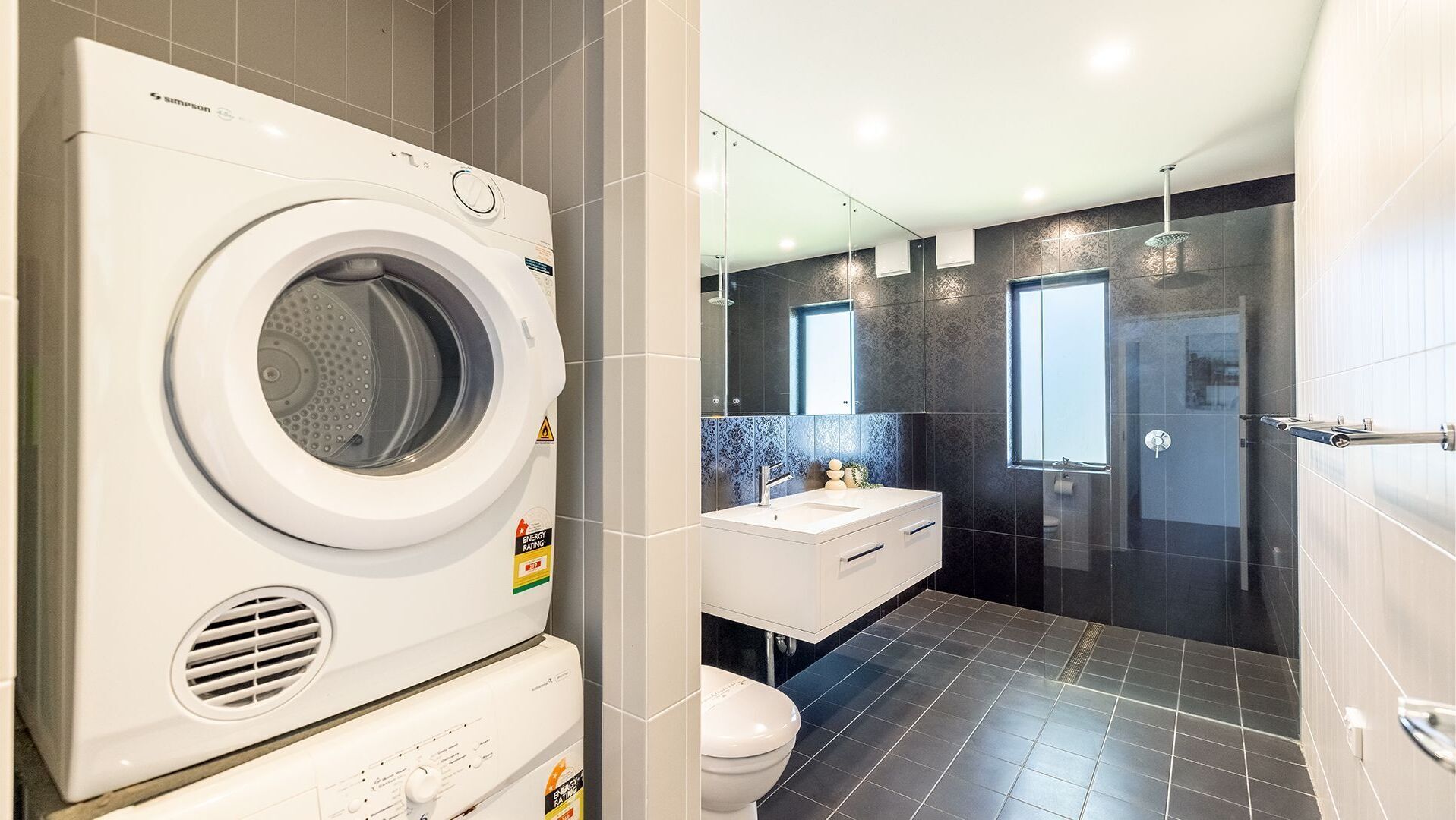 A modern bathroom with a built-in washing machine, a glass shower enclosure, and a vanity with a mirror.