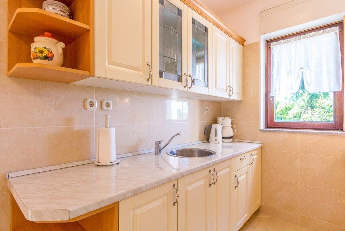 A kitchen with white cabinets, a marble countertop, a sink, a coffee maker, and a window with curtains.