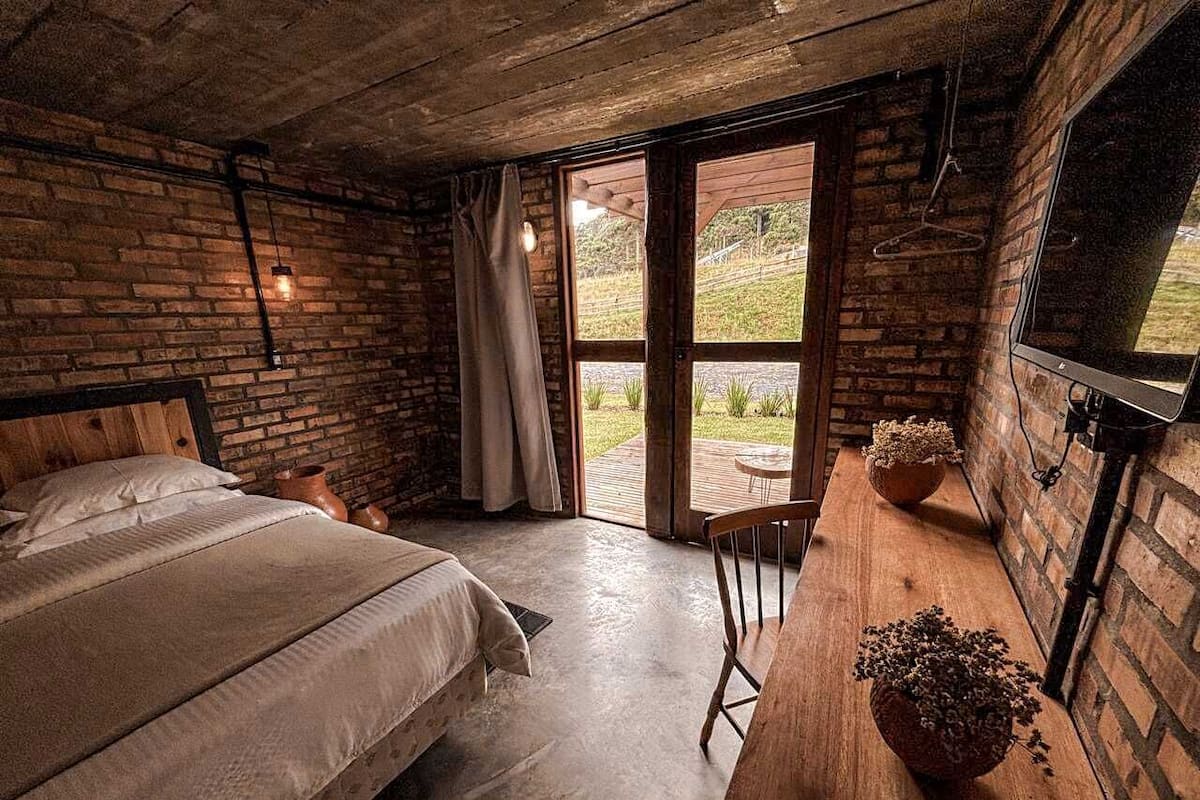 Ein rustikales Schlafzimmer mit einem großen Bett, einem hölzernen Schreibtisch und Blick ins Freie durch eine Glastür.