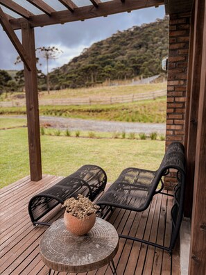 A wooden deck with two black wicker chairs and a round table with a potted plant. - Monte Sião Château (Urubici)