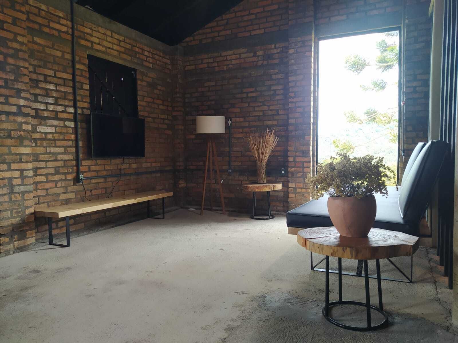A room with a brick wall, a bench, a table with a potted plant, a floor lamp, and a chair.