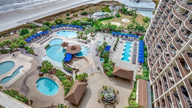 Een resort met meerdere zwembaden, ligbedden en een groot gebouw met balkons.