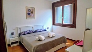 A bedroom with a bed, a nightstand, a lamp, a window with blinds, and a wall-mounted picture. - Mi casa es tu casa PN.Free Parking. Great location. (Pordenone)