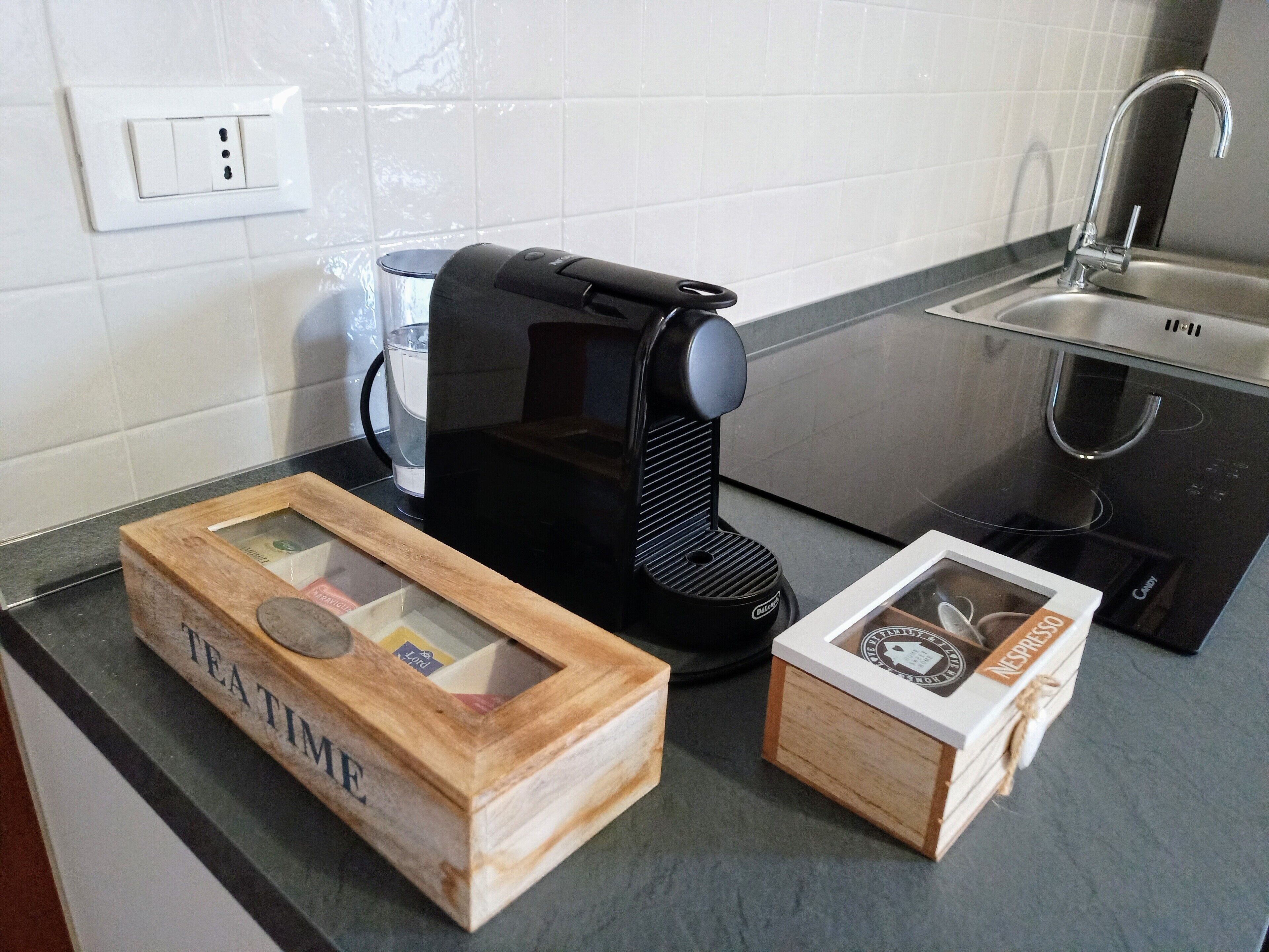 Una cocina con cafetera, un vaso de agua y dos cajas que dicen "TEATIME" y "NESPEUDO".
