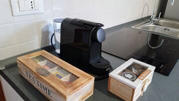 Una cocina con cafetera, un vaso de agua y dos cajas que dicen "TEATIME" y "NESPEUDO".