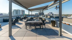 En tagterrasse med udendørs siddepladser, en pergola der giver skygge, og udsigt til byens skyline.