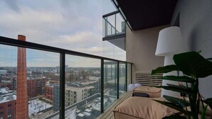 Un balcón moderno con vistas a la ciudad, una planta grande en maceta y un sofá con cojines.