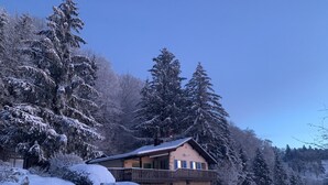 Een chalet met balkon, omringd door met sneeuw bedekte bomen en een heldere lucht.