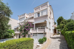 A multi-story residential building with balconies, a driveway, and a well-maintained garden.