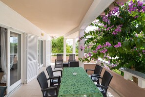 A covered outdoor dining area with a table and chairs, a pergola with climbing plants, and sliding glass doors.